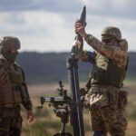 A Ukrainian soldier loads a mortar shell under the supervision of a French army instructor (L) during a military training with French servicemen, in a military training compound at an undisclosed location in Poland