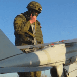 A Russian soldier standing next to an Orlan-10 uncrewed aerial reconnaissance vehicle. Photo via Wikimedia.